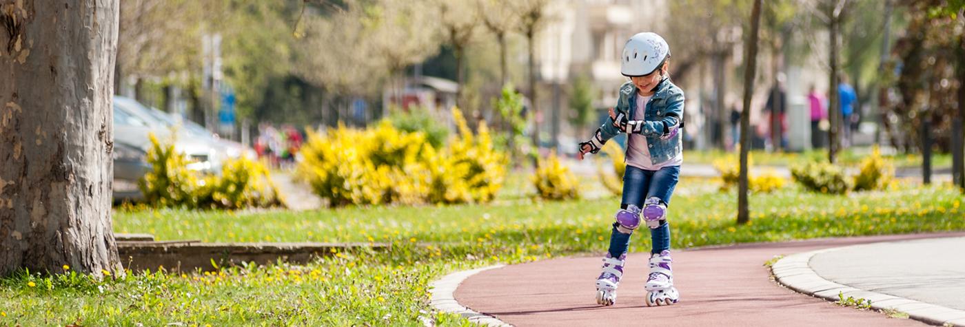 一个小女孩戴着护膝、护肘和头盔，在公园里滑旱冰。